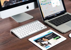 A sleek office desk setup featuring Apple devices: iMac, MacBook, and iPad.