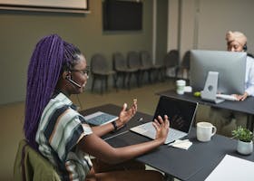 African-American woman working at laptop with headset in office, focused on communication.